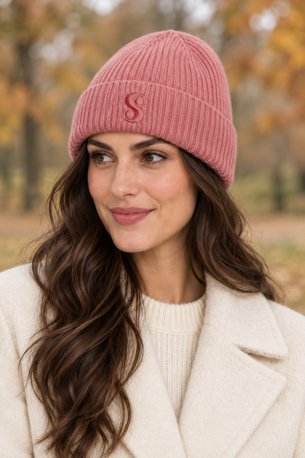 Woman wearing a dusty pink s.Oliver ribbed beanie with a cream coat in an autumn park.